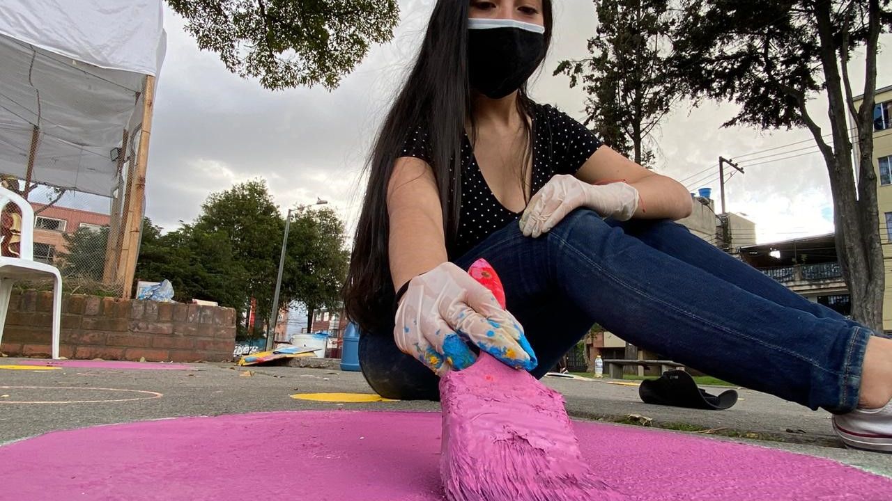 niña pintando de color rosa el piso en parque